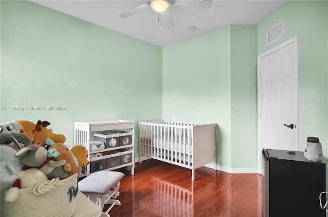 bedroom featuring wood-type flooring, a nursery area, and ceiling fan