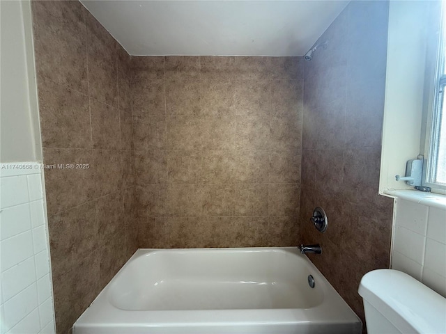 bathroom with tile walls, tiled shower / bath combo, and toilet