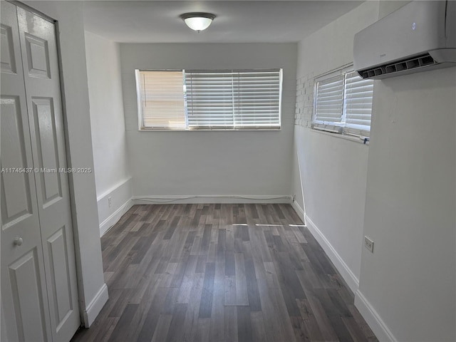 unfurnished bedroom featuring baseboards, a wall mounted AC, and dark wood-type flooring