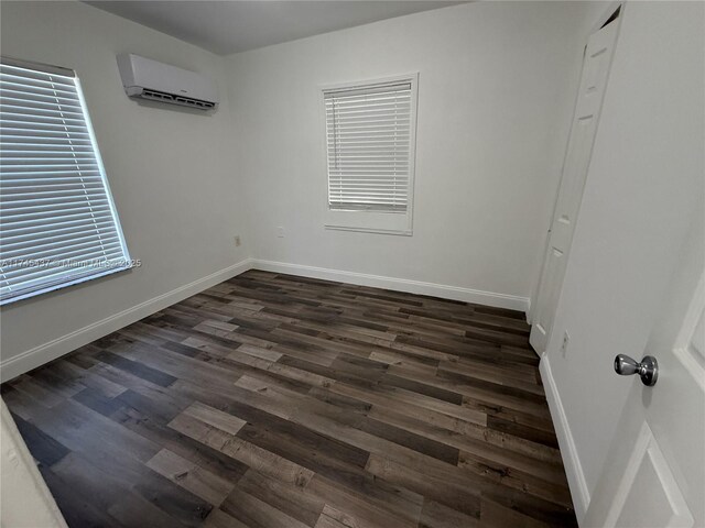 unfurnished room with dark wood-style floors, a wall mounted air conditioner, and baseboards