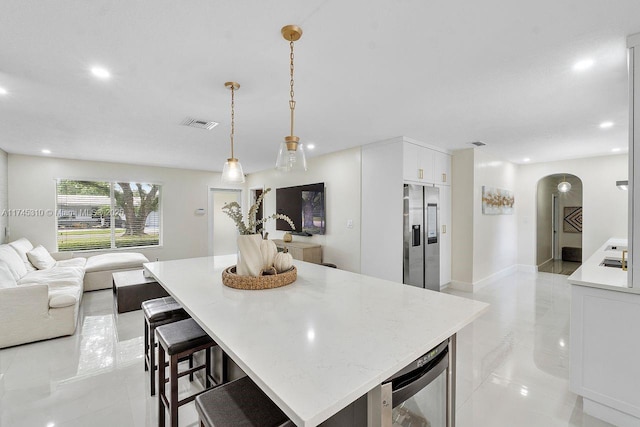 kitchen with a center island, stainless steel fridge with ice dispenser, pendant lighting, beverage cooler, and white cabinets