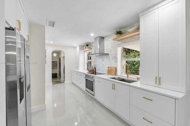 kitchen featuring wall chimney exhaust hood, appliances with stainless steel finishes, sink, and white cabinets