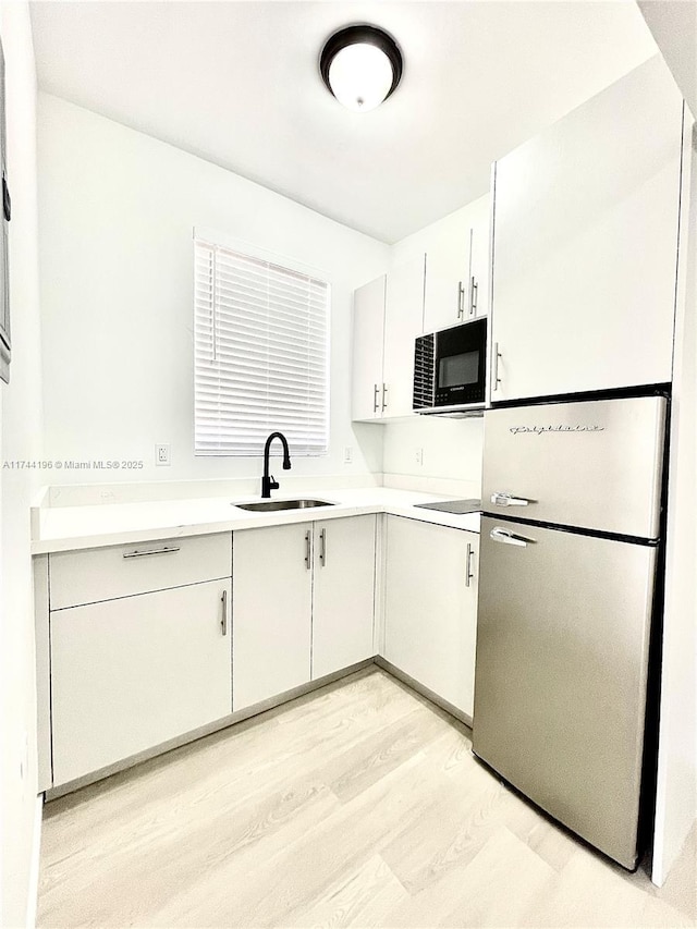 kitchen with sink, black appliances, light hardwood / wood-style floors, and white cabinets