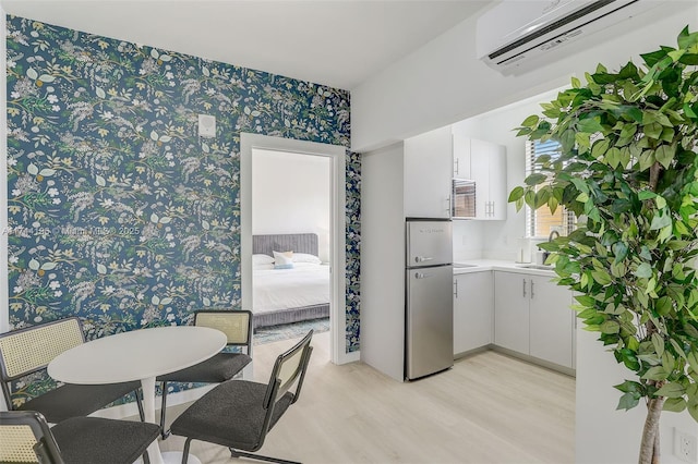 kitchen with white cabinetry, a wall mounted air conditioner, stainless steel fridge, and light wood-type flooring