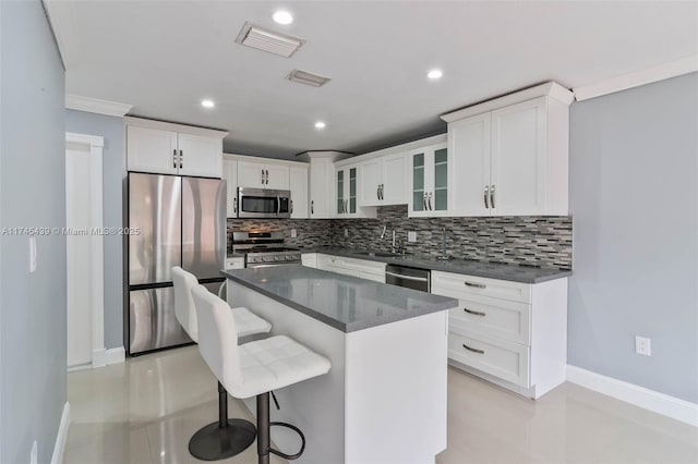 kitchen featuring stainless steel appliances, white cabinets, decorative backsplash, a breakfast bar, and a kitchen island