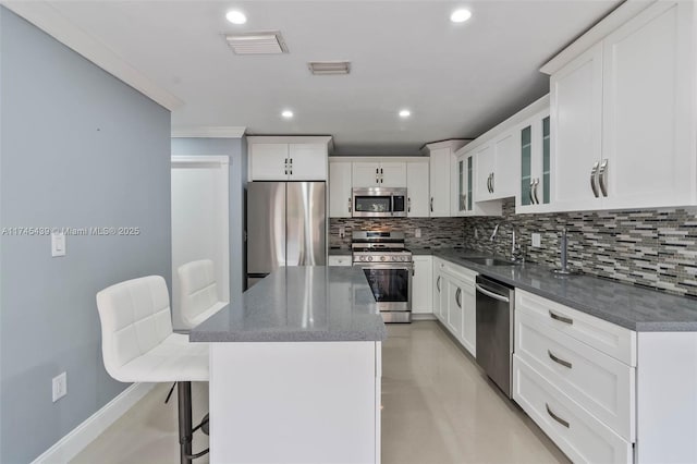 kitchen with a kitchen breakfast bar, stainless steel appliances, a kitchen island, sink, and white cabinetry