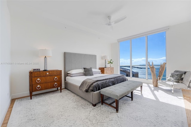 bedroom with a wall of windows, ceiling fan, a water view, light hardwood / wood-style floors, and access to outside