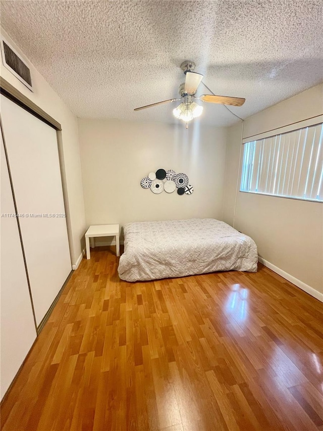 unfurnished bedroom featuring a closet, ceiling fan, light hardwood / wood-style floors, and a textured ceiling