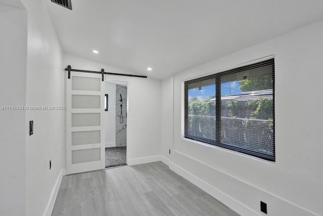 unfurnished bedroom featuring lofted ceiling, a barn door, recessed lighting, baseboards, and light wood-style floors