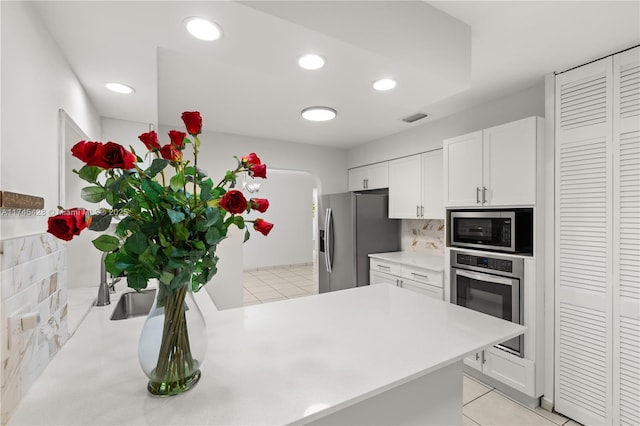 kitchen with stainless steel appliances, light tile patterned floors, decorative backsplash, and white cabinets