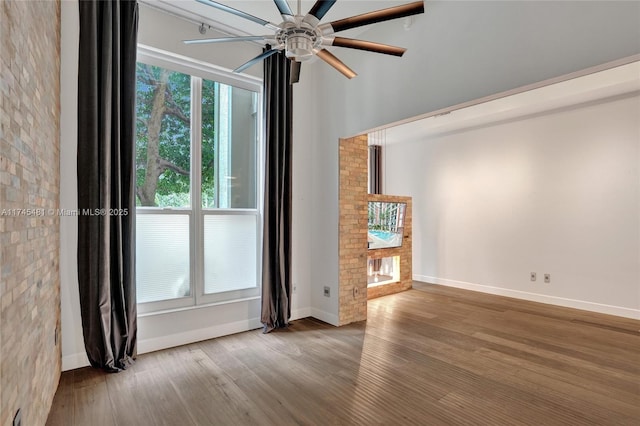 empty room featuring hardwood / wood-style flooring, a brick fireplace, and ceiling fan