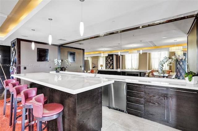 kitchen featuring refrigerator, dark brown cabinetry, a kitchen bar, decorative light fixtures, and light tile patterned flooring