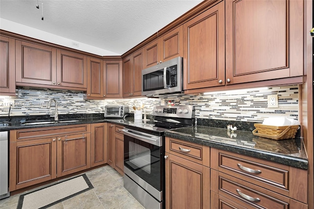 kitchen with sink, appliances with stainless steel finishes, backsplash, a textured ceiling, and dark stone counters