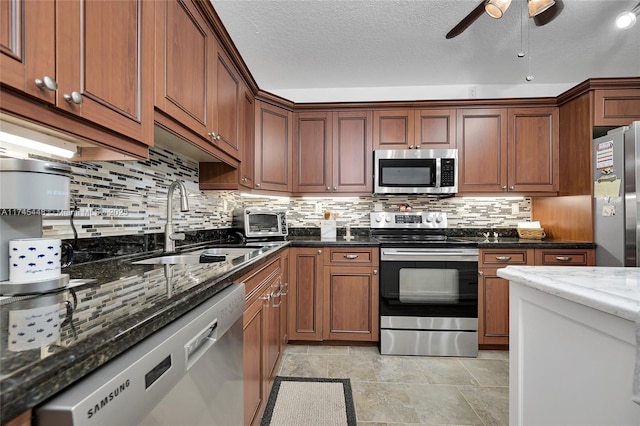 kitchen featuring sink, a textured ceiling, dark stone countertops, appliances with stainless steel finishes, and backsplash