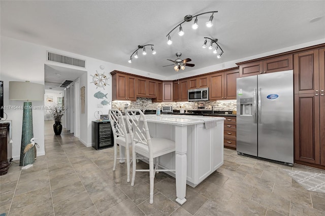 kitchen featuring beverage cooler, a kitchen breakfast bar, decorative backsplash, a center island, and stainless steel appliances