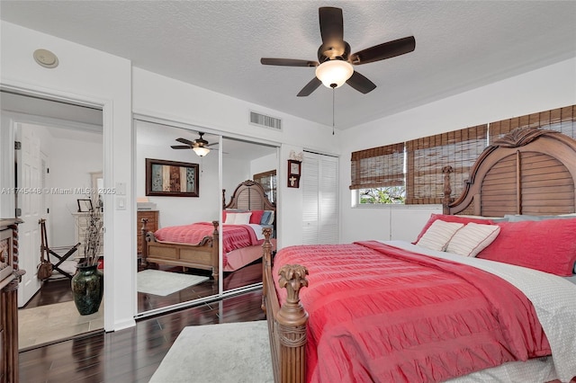 bedroom featuring dark wood-type flooring, ceiling fan, a textured ceiling, and two closets