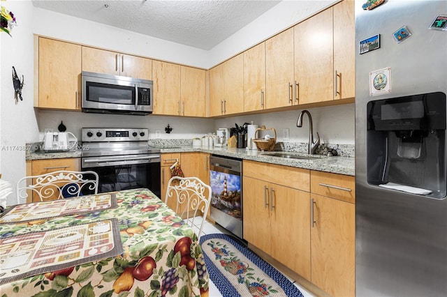 kitchen with sink, a textured ceiling, light brown cabinets, stainless steel appliances, and light stone countertops