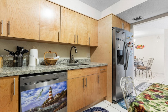 kitchen with appliances with stainless steel finishes, sink, light tile patterned floors, light stone countertops, and a textured ceiling