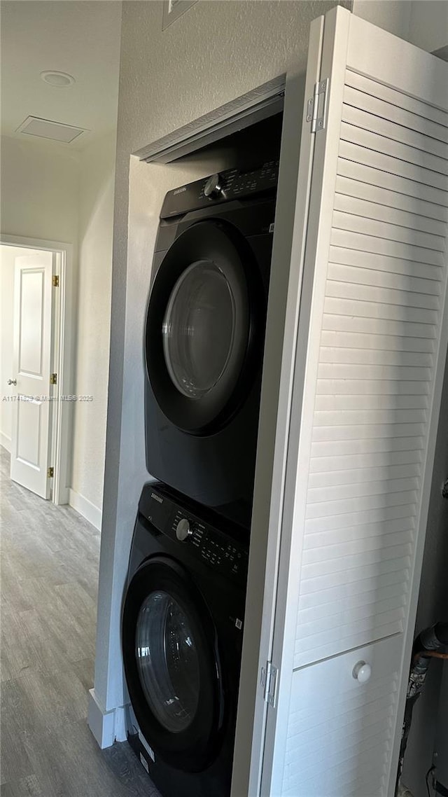 laundry room with hardwood / wood-style flooring and stacked washing maching and dryer