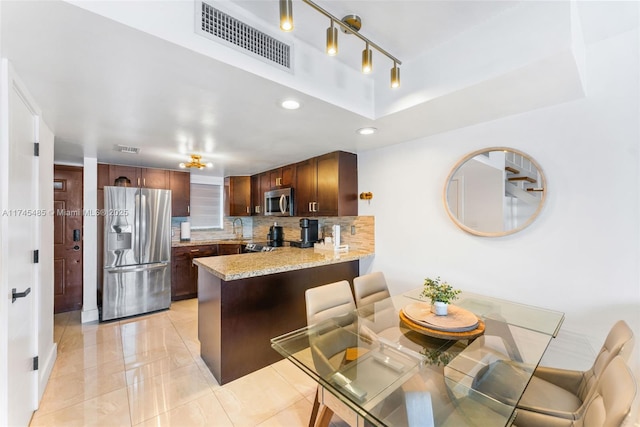 kitchen with sink, appliances with stainless steel finishes, kitchen peninsula, light stone countertops, and backsplash