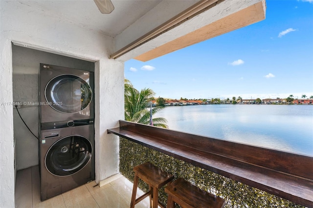 washroom featuring stacked washer and dryer, light tile patterned floors, and a water view