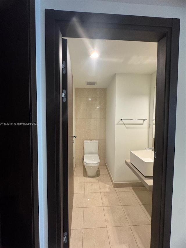 bathroom with toilet, tile patterned flooring, sink, and tile walls