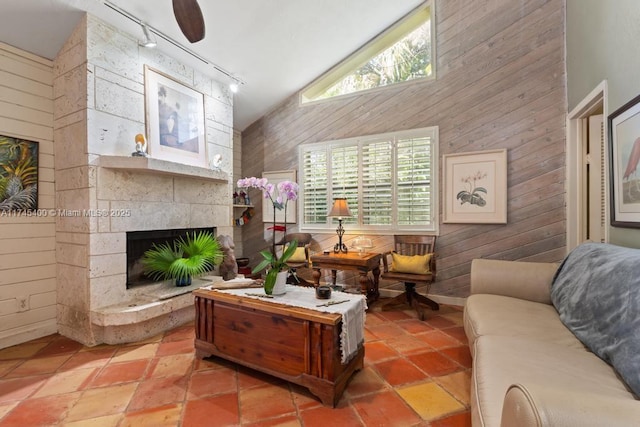 living area featuring track lighting, lofted ceiling, wood walls, and a fireplace