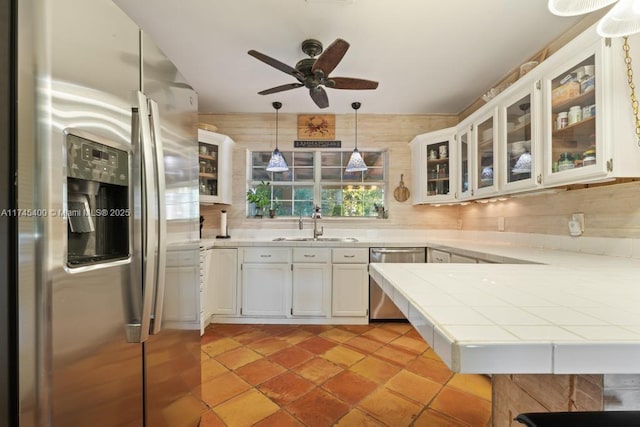 kitchen featuring a ceiling fan, a sink, appliances with stainless steel finishes, white cabinets, and tile counters