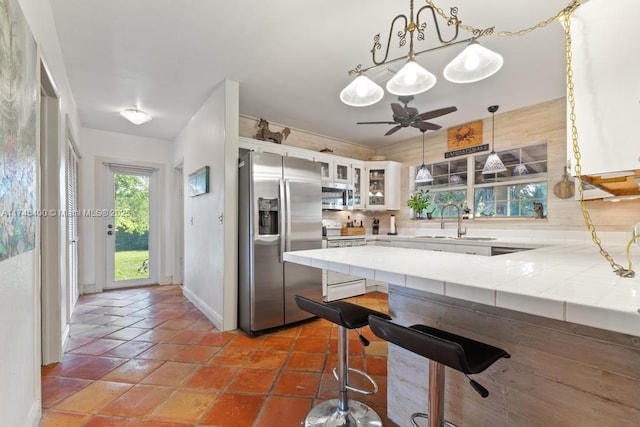 kitchen with tile countertops, appliances with stainless steel finishes, a peninsula, white cabinetry, and a sink