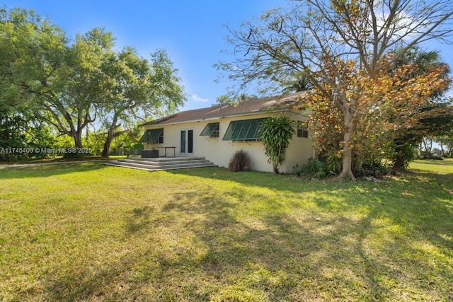 rear view of house with stucco siding and a lawn