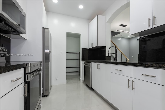 kitchen featuring appliances with stainless steel finishes, tasteful backsplash, white cabinetry, sink, and dark stone countertops