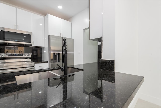 kitchen featuring appliances with stainless steel finishes, dark stone countertops, backsplash, white cabinetry, and kitchen peninsula