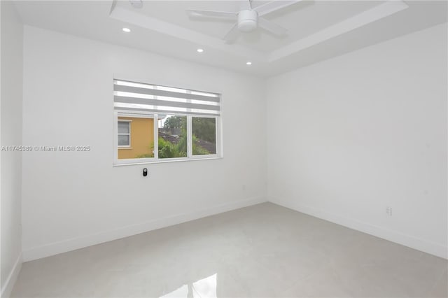 spare room featuring ceiling fan, a tray ceiling, and concrete flooring