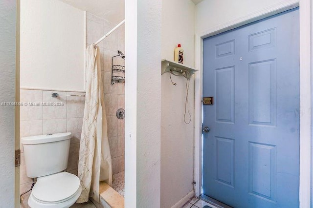 bathroom with toilet, curtained shower, and tile walls