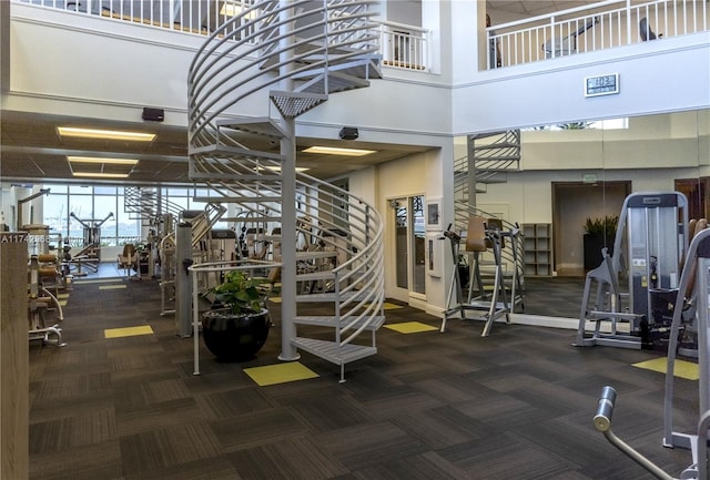 exercise room featuring a towering ceiling and dark colored carpet