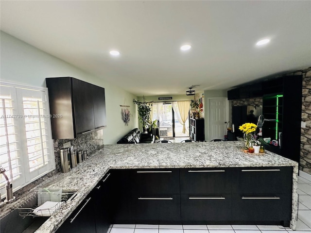 kitchen with sink, light stone countertops, kitchen peninsula, and backsplash