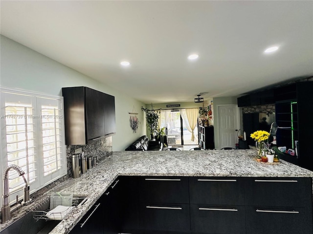 kitchen with sink, decorative backsplash, kitchen peninsula, and light stone counters