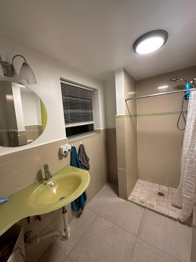 bathroom with tile walls, tiled shower, wainscoting, tile patterned flooring, and a sink