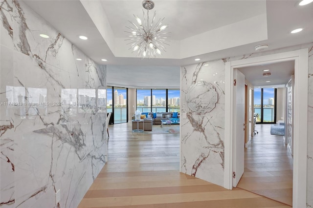 hallway with floor to ceiling windows, tile walls, an inviting chandelier, and light hardwood / wood-style floors