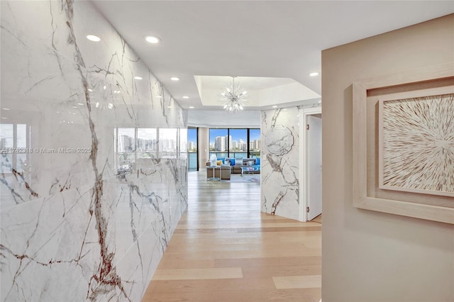 corridor with a tray ceiling, a chandelier, and light hardwood / wood-style floors