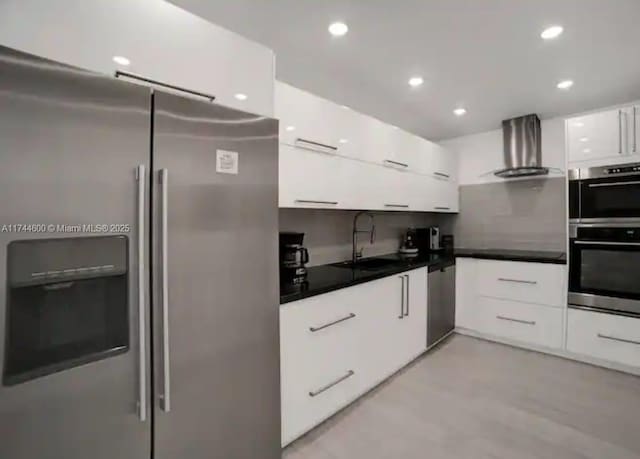 kitchen with wall chimney exhaust hood, white cabinetry, stainless steel appliances, and sink