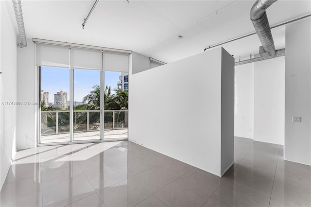 spare room featuring tile patterned flooring, a view of city, and a wall of windows