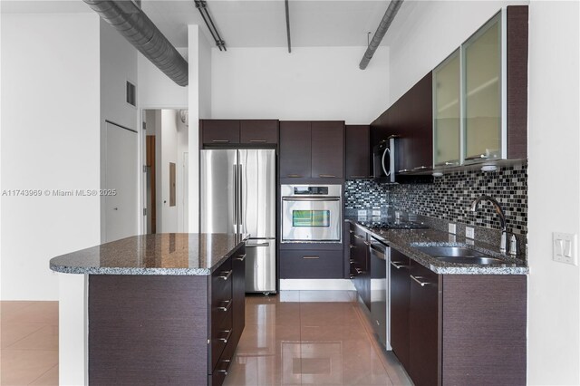 kitchen featuring dark brown cabinetry, stainless steel appliances, a sink, a center island, and tasteful backsplash