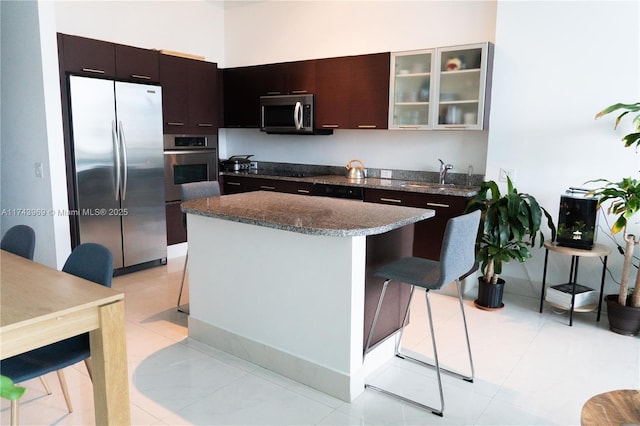 kitchen with light tile patterned floors, dark stone counters, glass insert cabinets, a center island, and stainless steel appliances