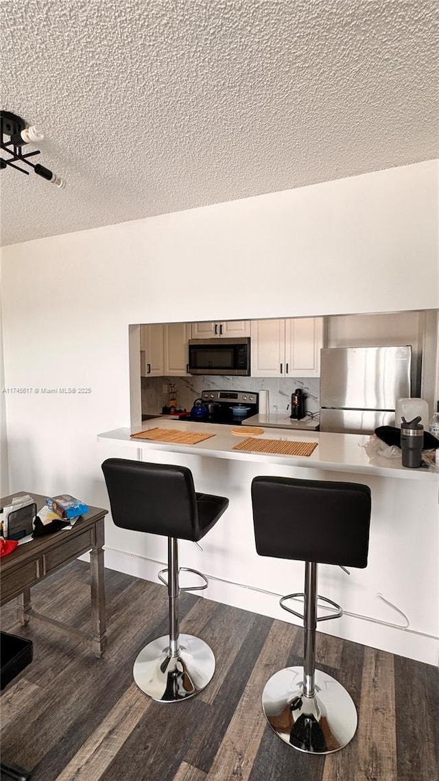 kitchen with a breakfast bar, a textured ceiling, stainless steel appliances, hardwood / wood-style floors, and backsplash