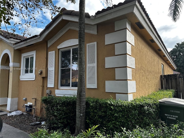 view of property exterior with a tile roof, fence, and stucco siding