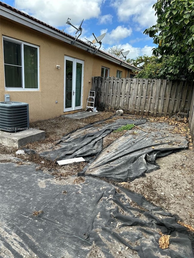 exterior space featuring french doors, stucco siding, fence, and central AC unit