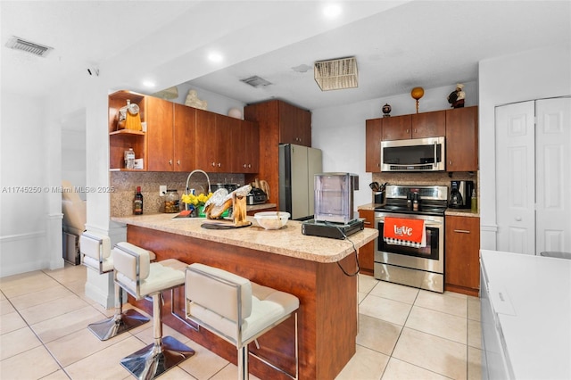 kitchen with a kitchen breakfast bar, a peninsula, light countertops, backsplash, and appliances with stainless steel finishes