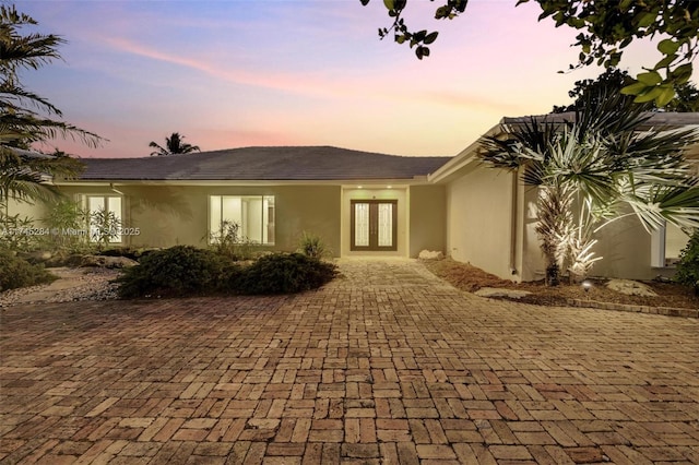 back of property at dusk featuring french doors and stucco siding