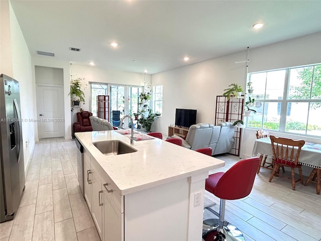 kitchen with sink, stainless steel appliances, light stone countertops, an island with sink, and white cabinets